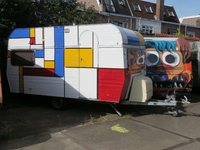 833737 Afbeelding van een in Mondriaanstijl beschilderde caravan op het parkeerterrein bij een loods van SWK-Creatieve ...